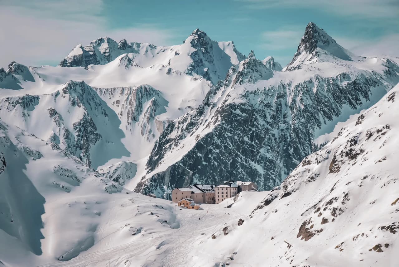 Paysage alpin majestueux au col du Grand-Saint-Bernard, refuge enneigé entouré de sommets époustouflants.