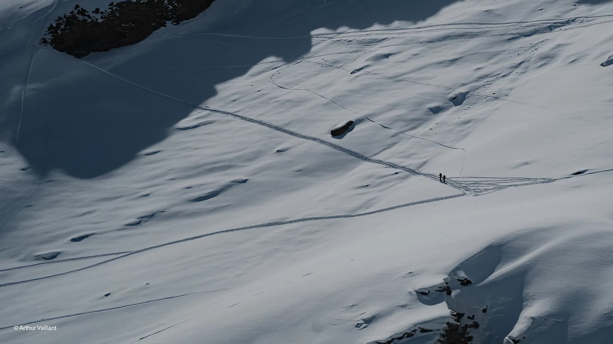 Two skiers are making their way across a snow-covered Alpine landscape, bathed in sunlight.