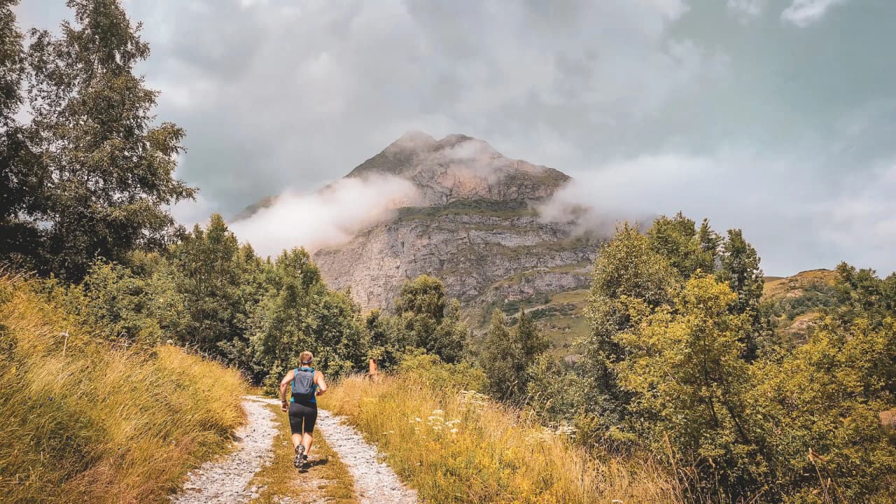 Un coureur de trail s'élance sur un chemin de terre vers une montagne imposante et embrumée, entouré d'une végétation sauvage