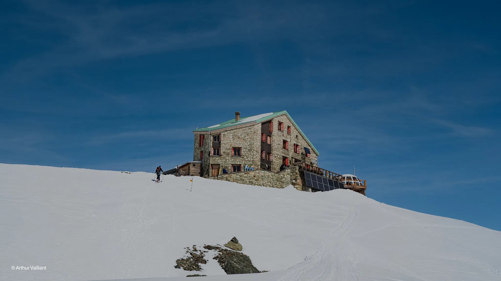 A mountain hut nestled amongst the glaciers, beneath a blue sky, beckoning you to embark on an alpine adventure.