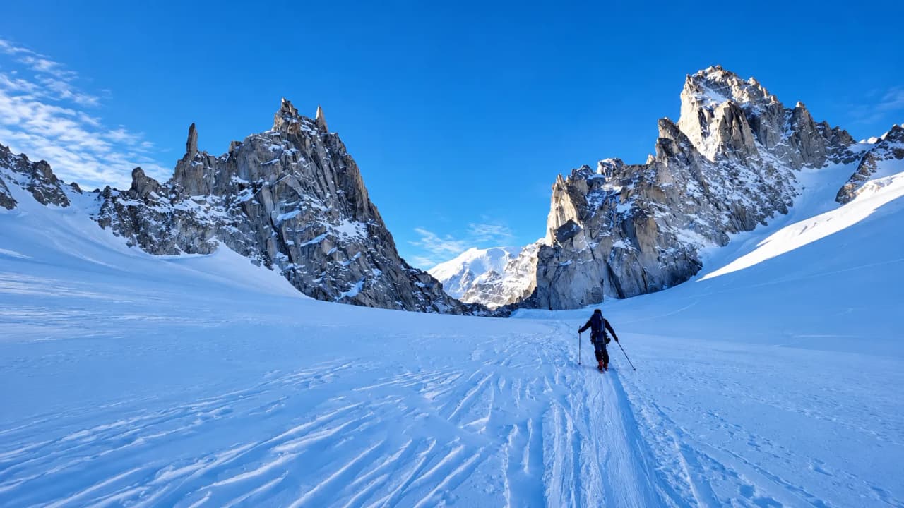 A ski tourer is crossing a vast, snow-covered alpine landscape, surrounded by majestic mountains.
