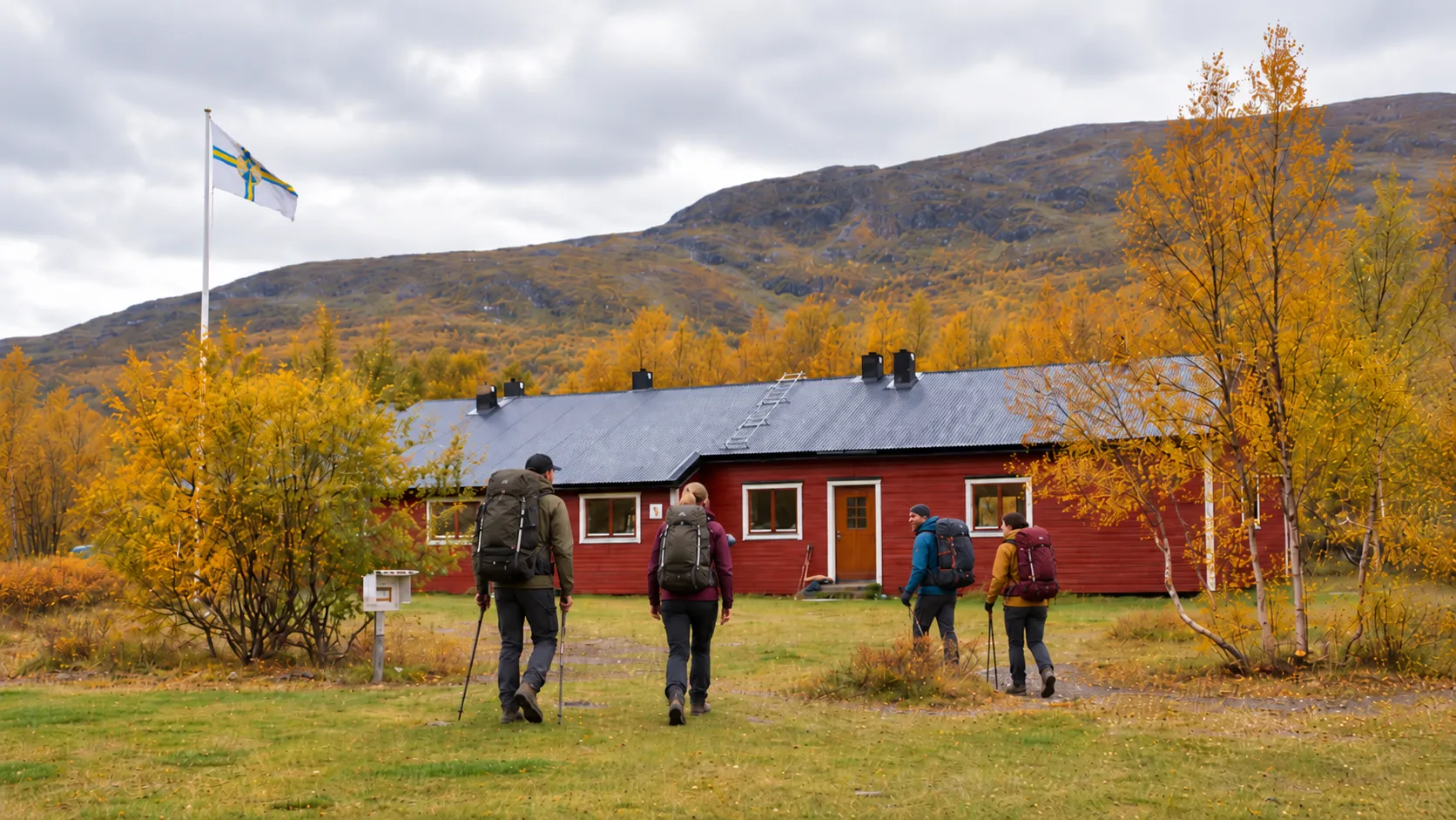 Een groep wandelaars in Lapland, op weg naar een rood huisje onder een bewolkte hemel.