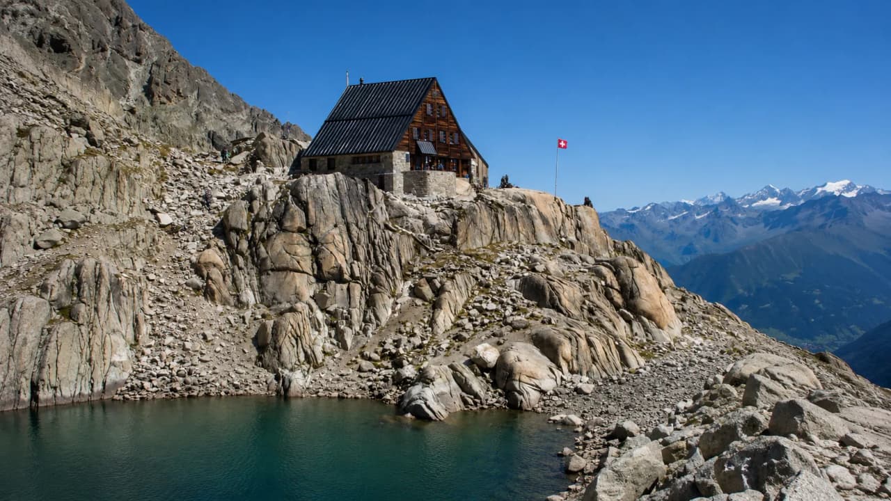 An alpine Mountain hut overlooking a turquoise lake, with majestic mountains in the background.
