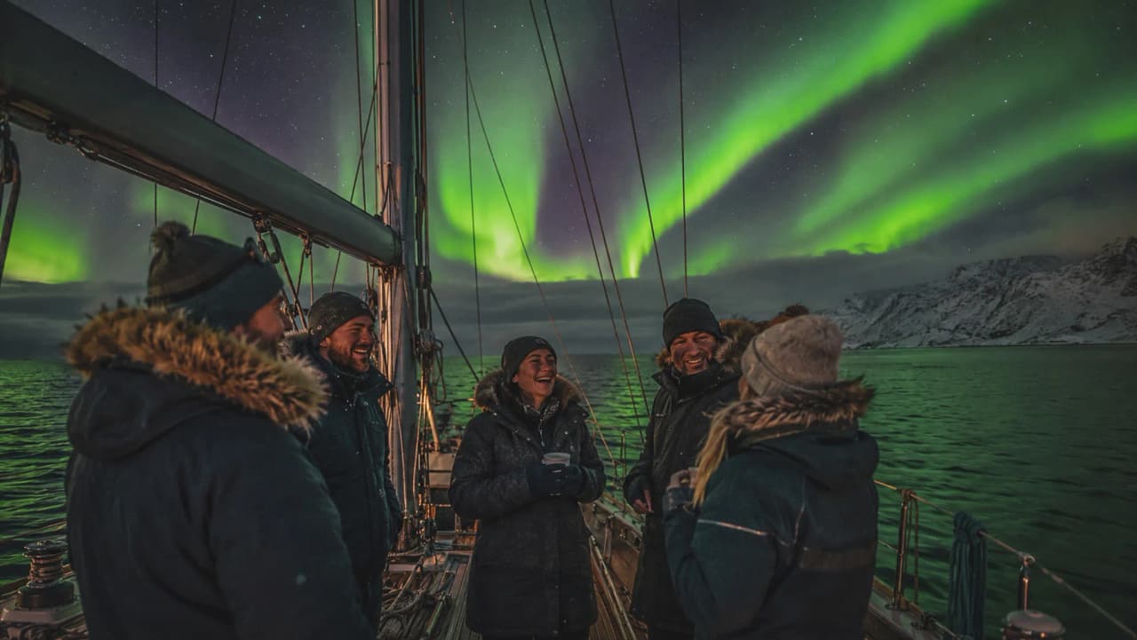 Vijf vrolijke mensen op een zeilboot, onder het noorderlicht in een Noorse fjord.