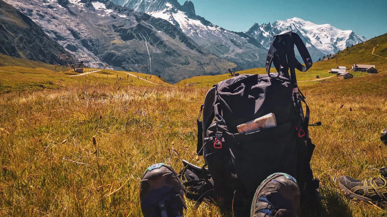 Een rugzak op het gras, met majestueuze Alpentoppen op de achtergrond.