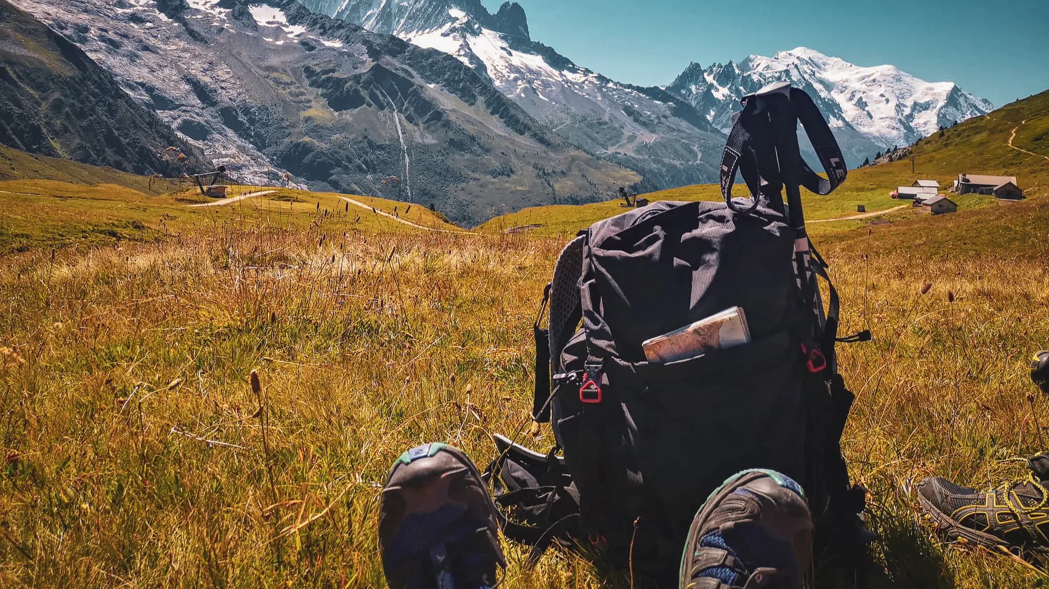 Een rugzak op het gras, met majestueuze Alpentoppen op de achtergrond.