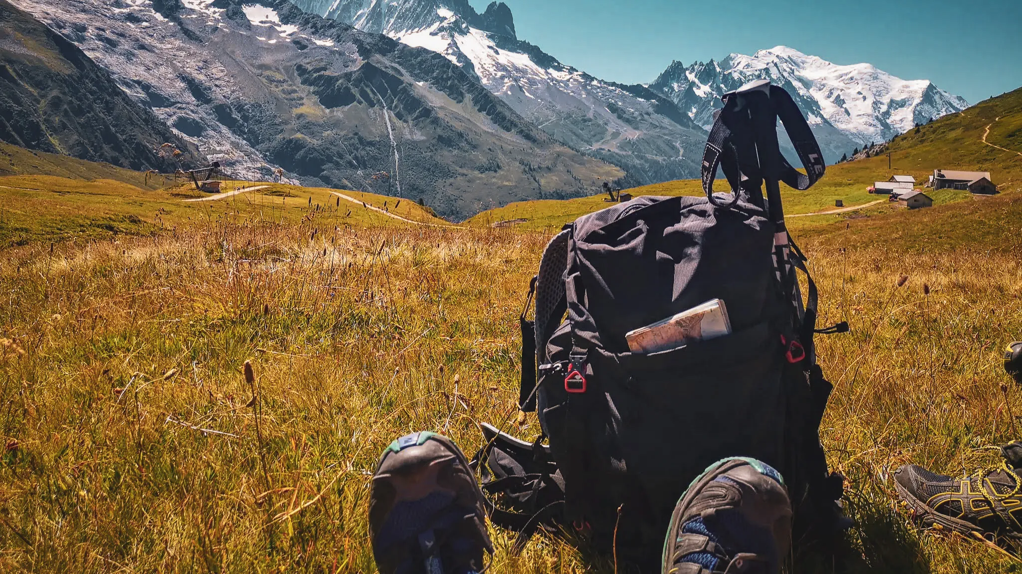 Een rugzak op het gras, met majestueuze Alpentoppen op de achtergrond.