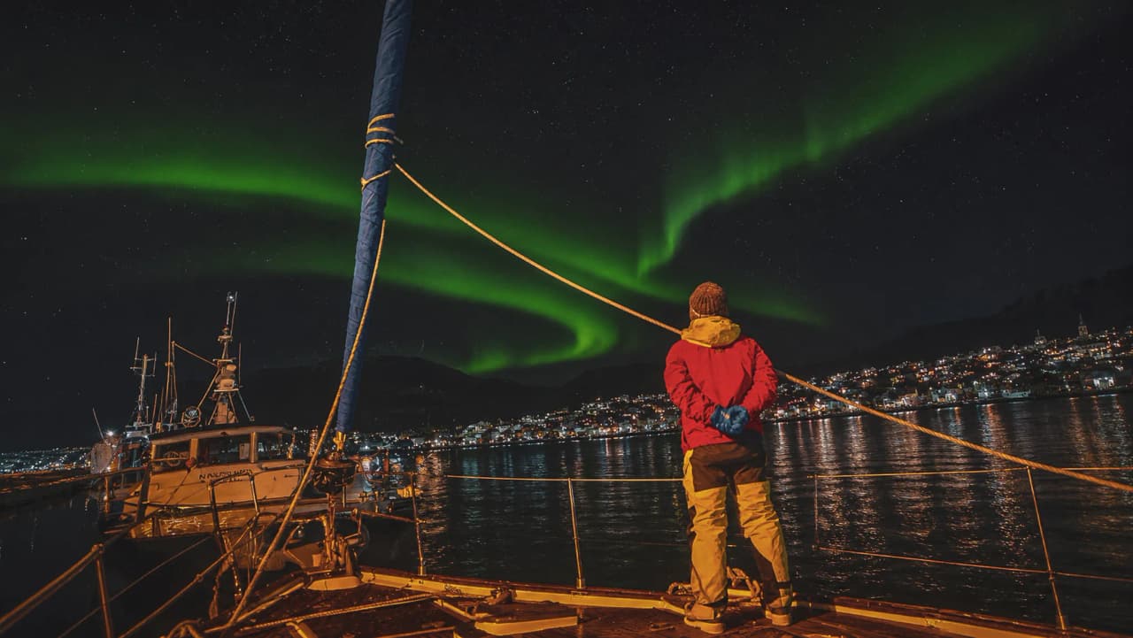 Een zeeman die vanaf een zeilboot in de fjorden van Tromsø naar het noorderlicht kijkt.