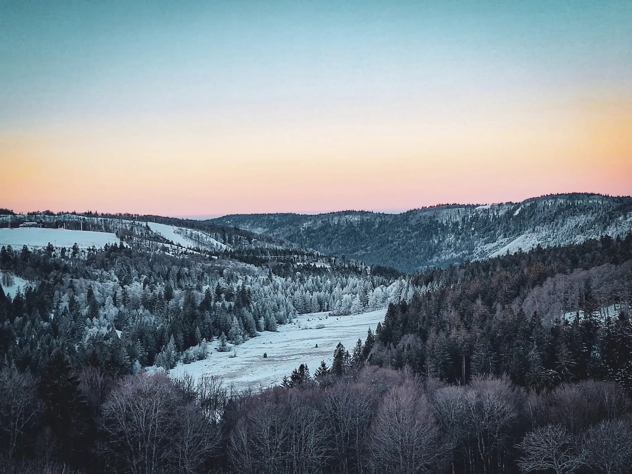 A panoramic winter view of the Vosges, with snow-covered hills and a soothing pastel sky.