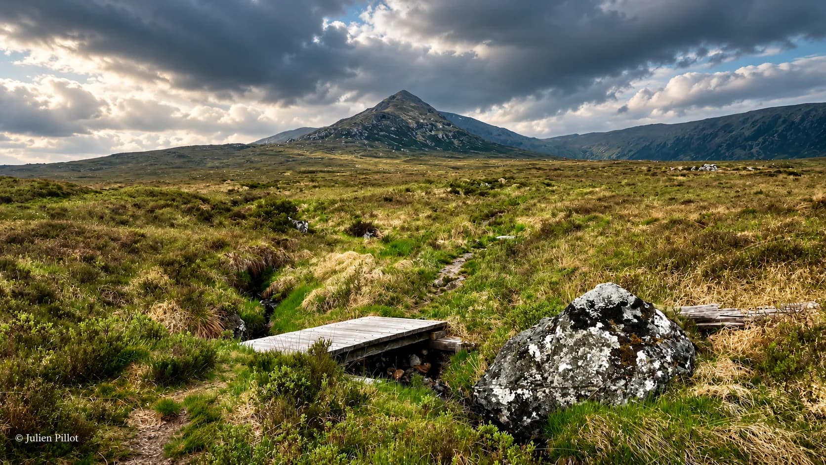 Een ruig Schots landschap, met een majestueuze bergtop, groene weiden en indrukwekkende wolken.