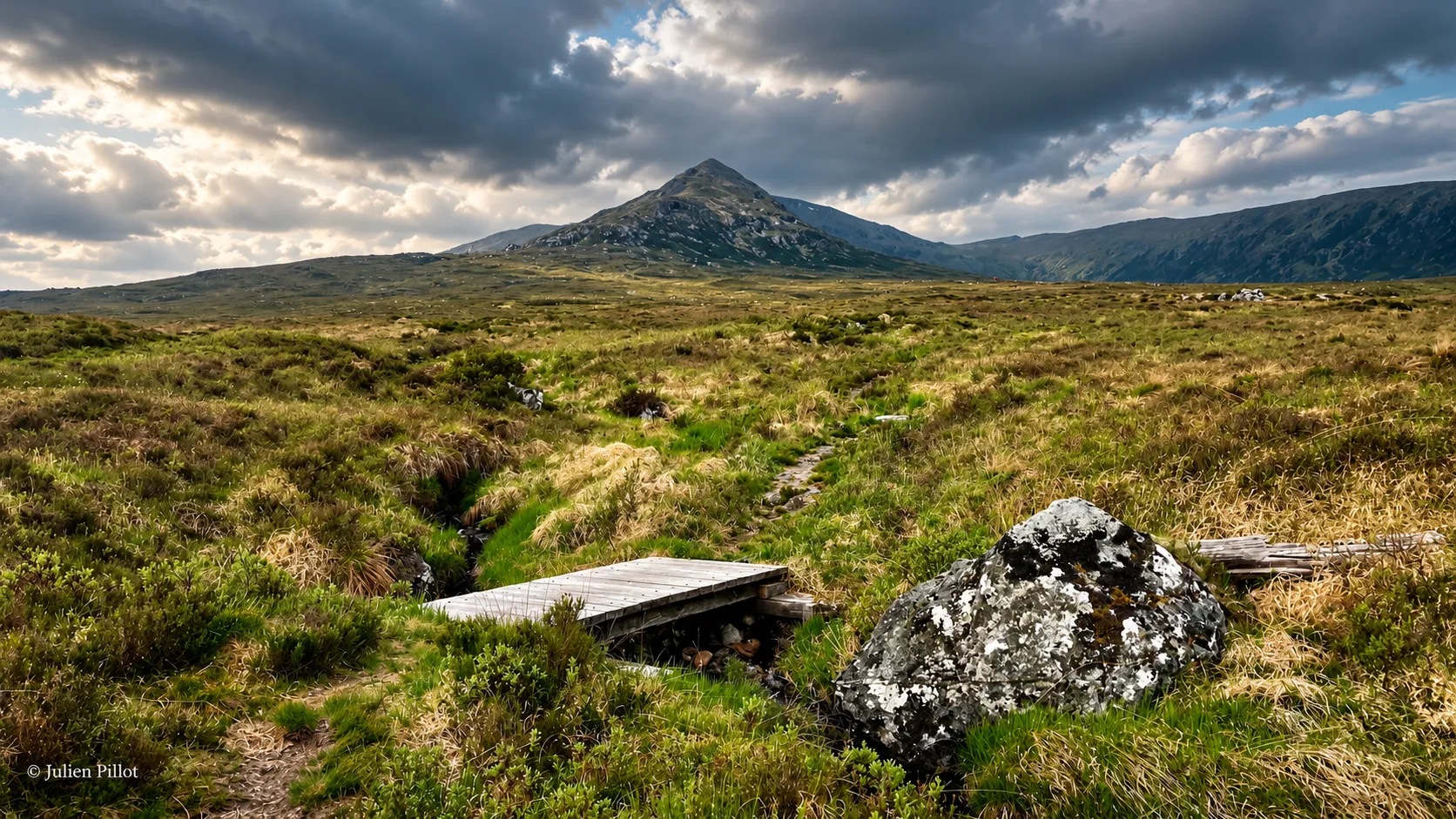 Een ruig Schots landschap, met een majestueuze bergtop, groene weiden en indrukwekkende wolken.