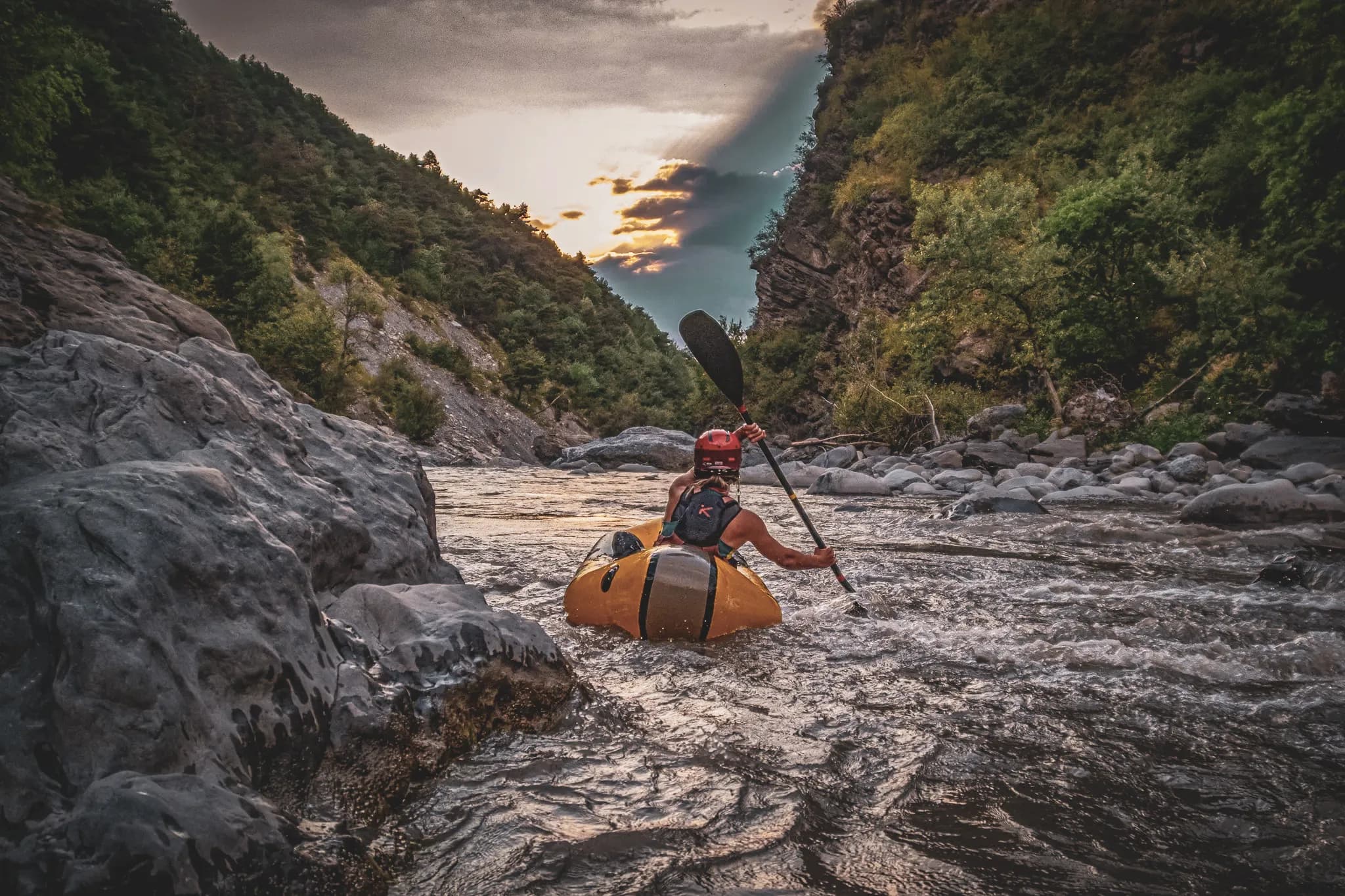 A packraft adventurer gliding along the Ubaye river, surrounded by lush green cliffs.