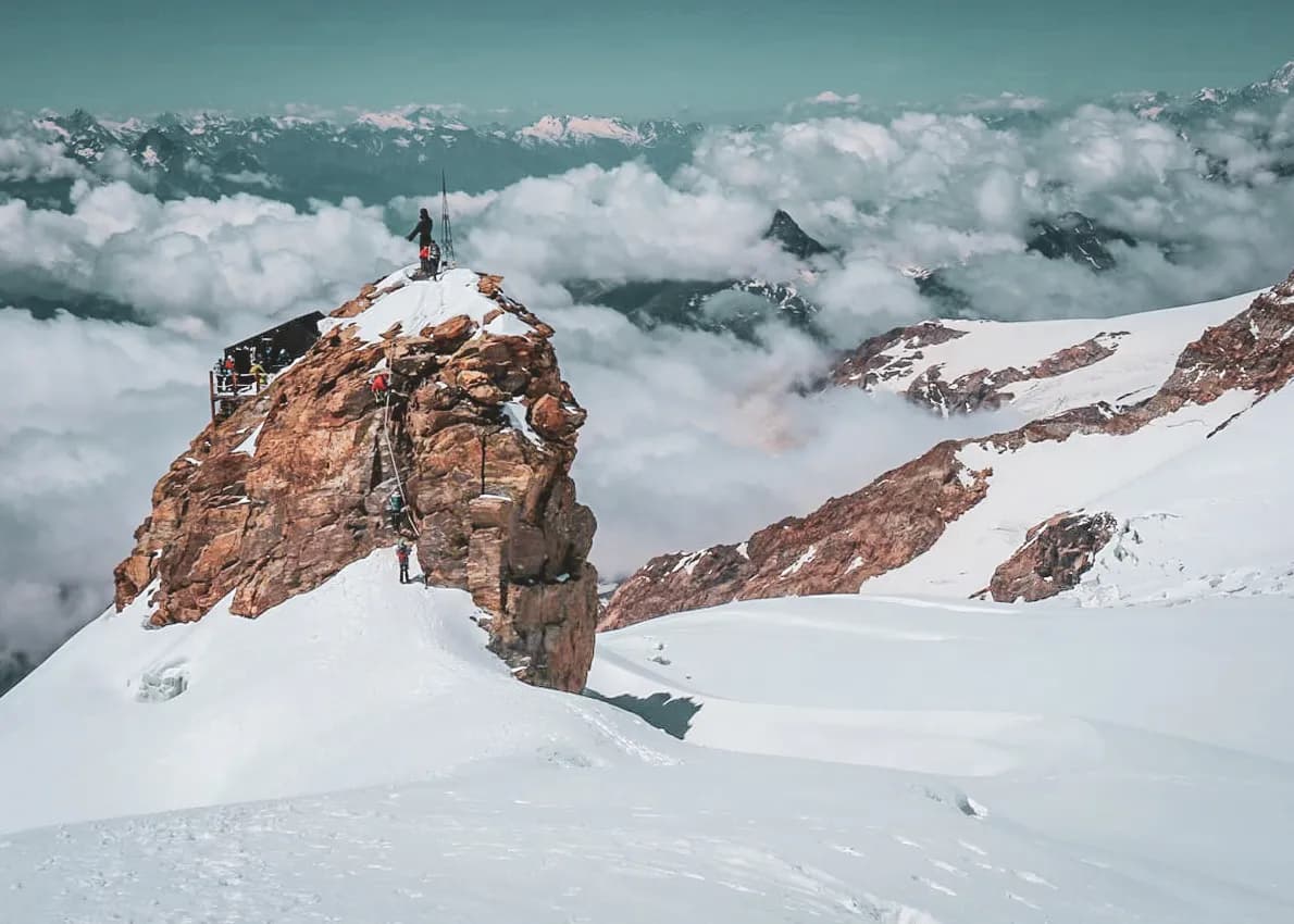 Montagne enneigée du Mont Rose, randonneurs sur un sommet majestueux entouré de nuages.
