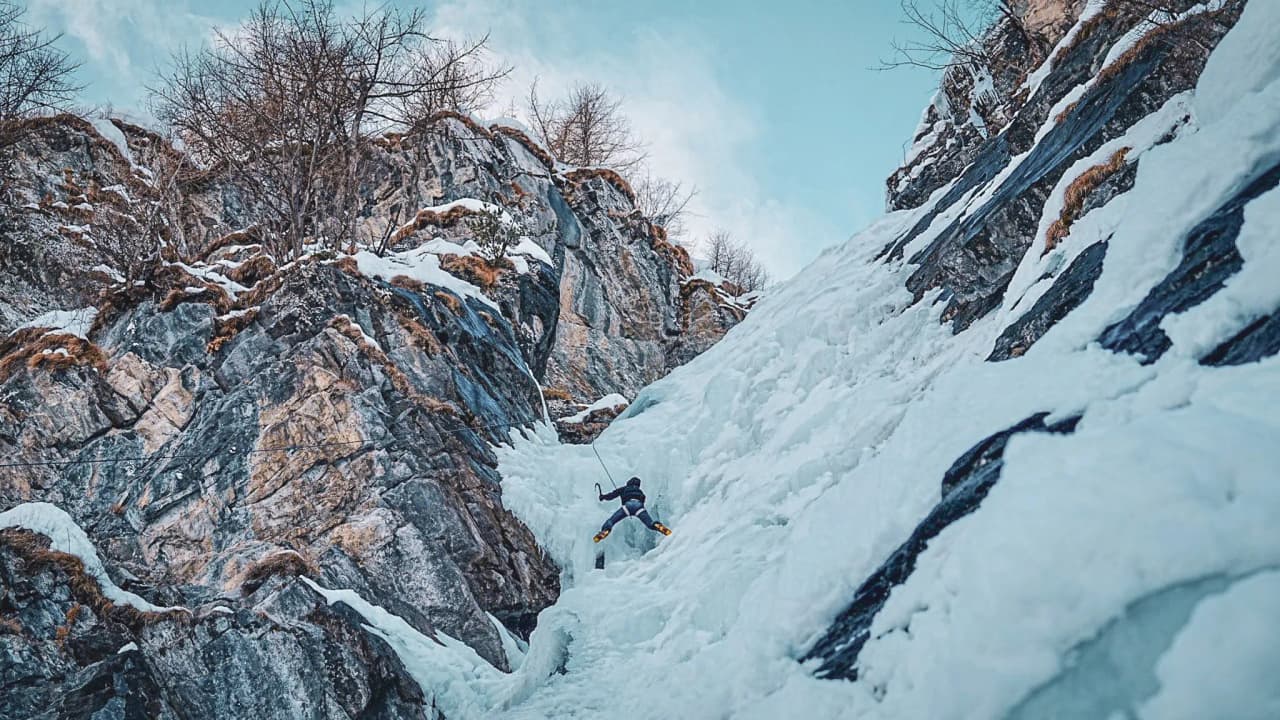 A climber tackles an ice wall in a breathtaking Alpine landscape.