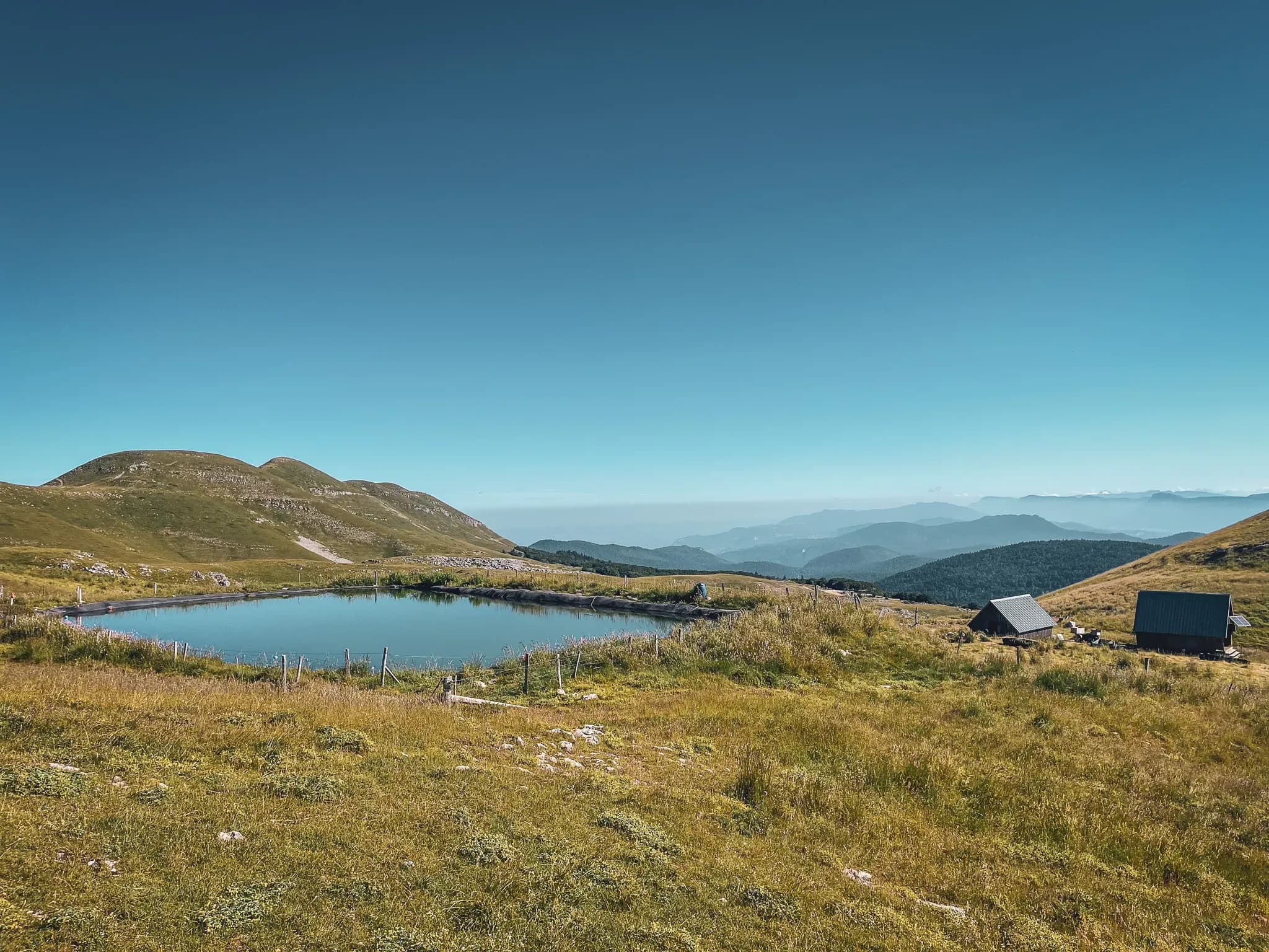 A peaceful pond surrounded by green hills, under a brilliant blue sky in the Vercors.