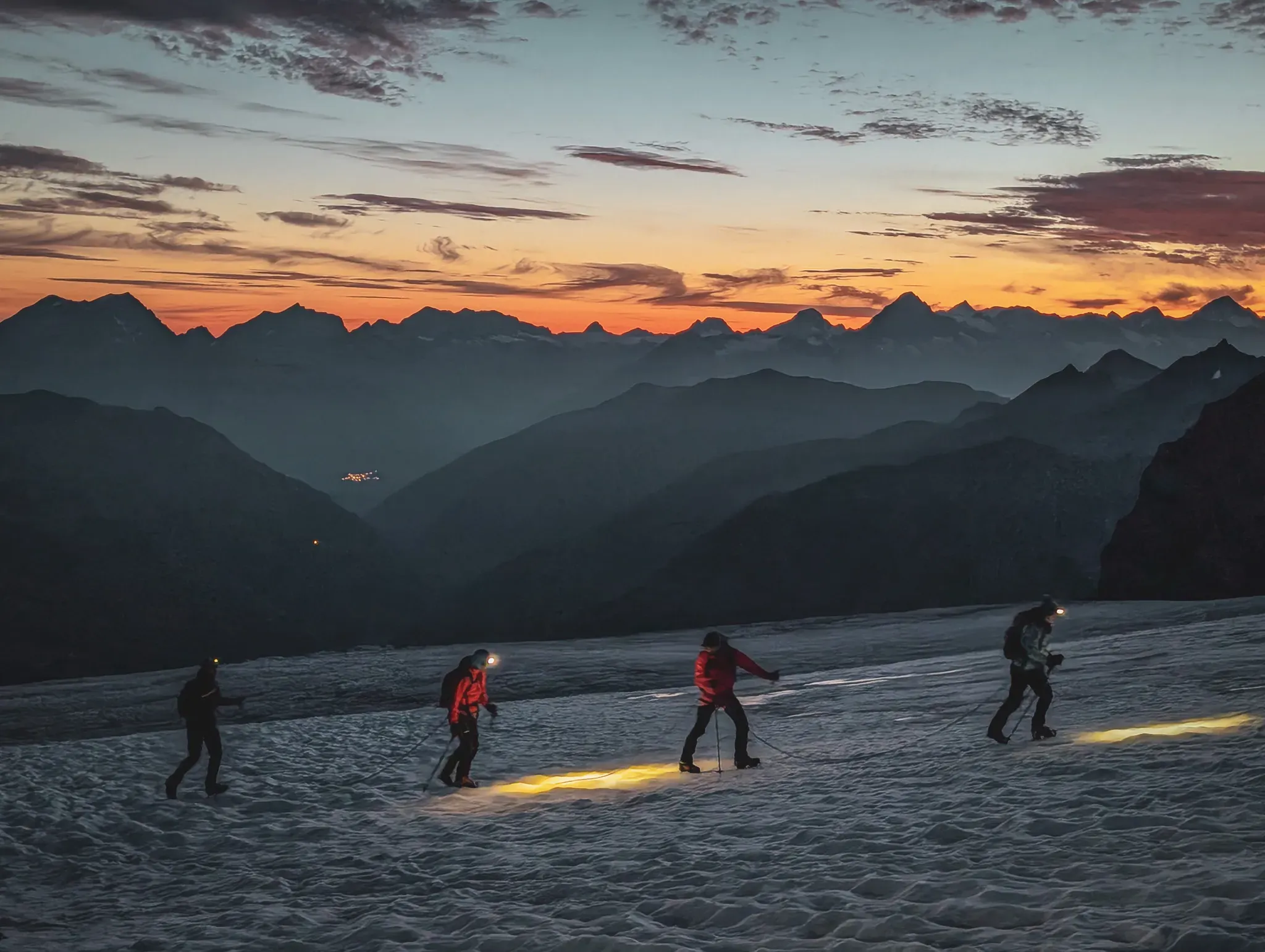 Mountaineers crossing a glacier at dusk, with majestic mountains in the background.