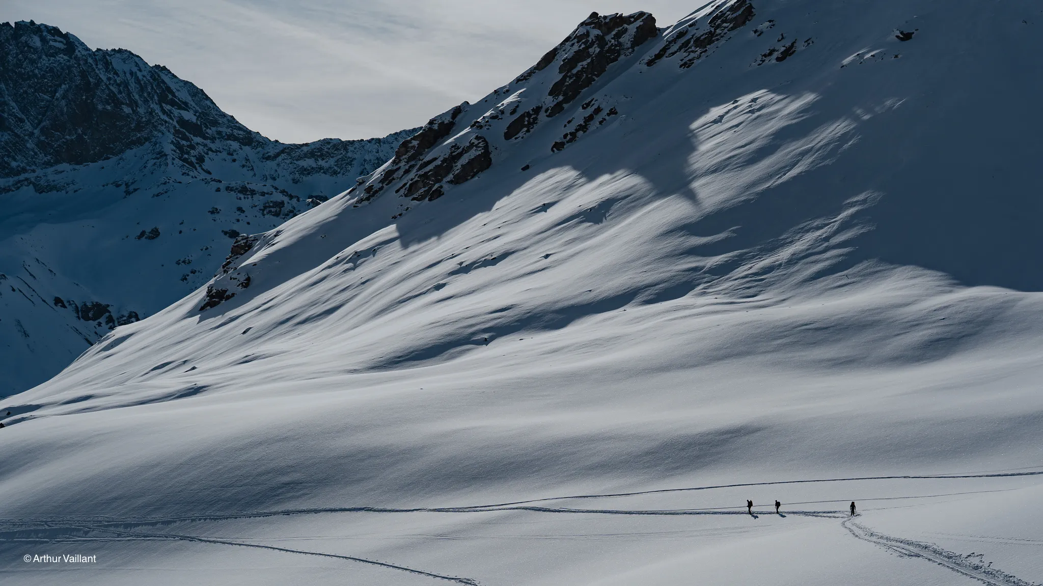 Three adventurers make their way through a pristine alpine landscape, amidst majestic mountains and glistening snow.