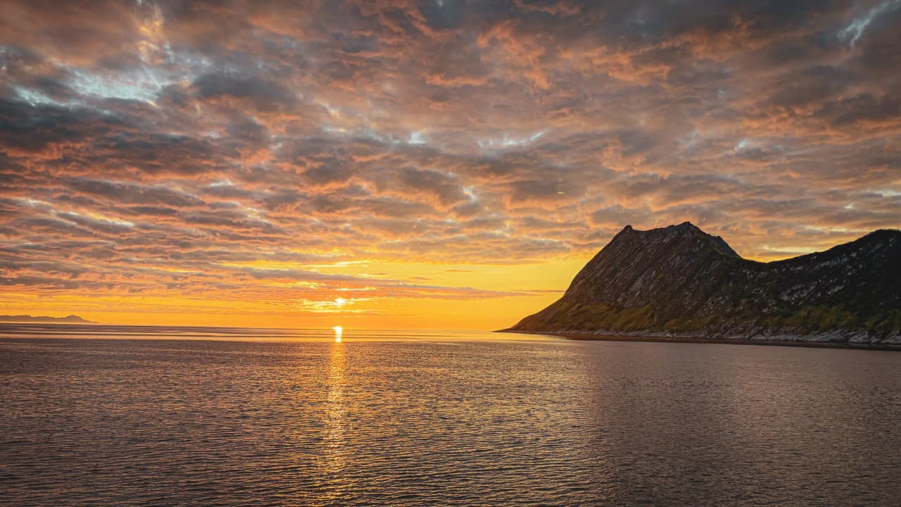 Zinderende zonsondergang op het eiland Senja, gouden reflectie op de kalme zee.