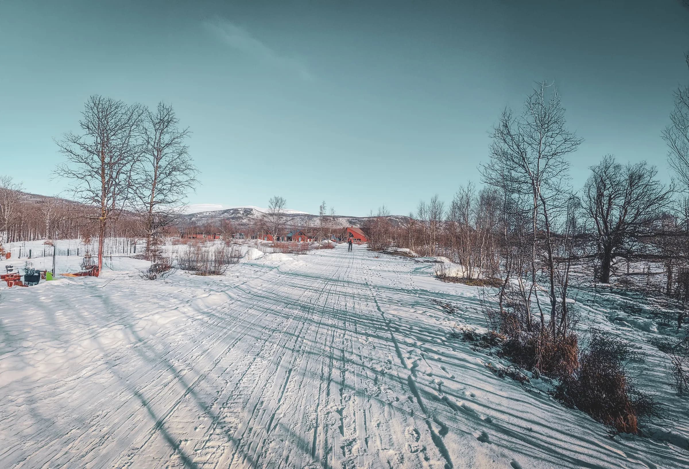 A snowy trail in the heart of Lapland, with mountains in the background and colourful huts.