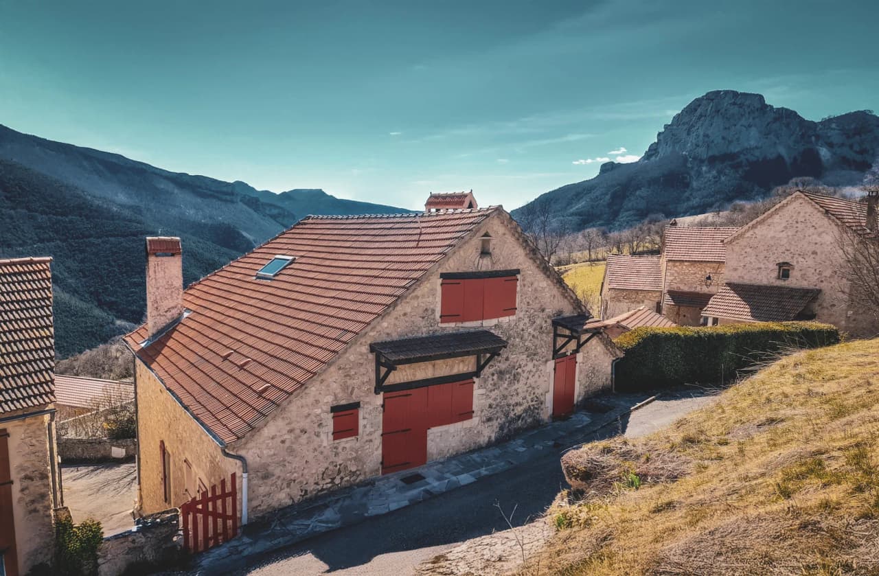 Stone house with red shutters, surrounded by majestic mountains and soothing countryside.