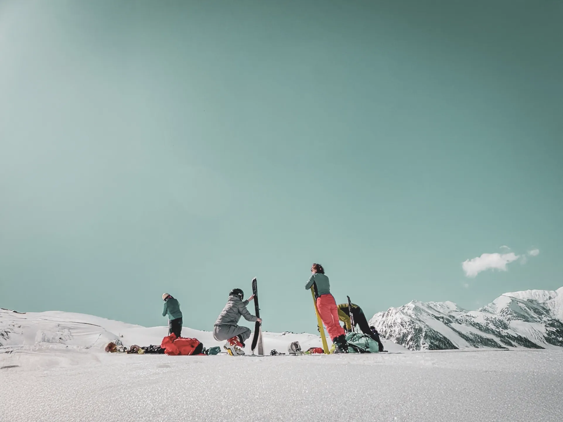 Groupe de skieurs sur un vaste glacier, montagnes en arrière-plan, ciel bleu et nuages légers.