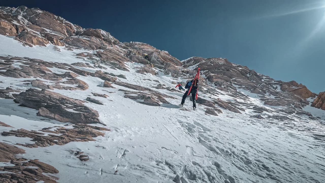 Trekking up glacial slopes, surrounded by majestic mountains under a blue sky.