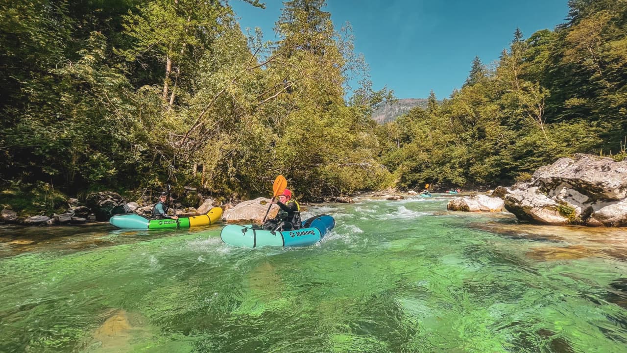 Packraft expedition on a crystal-clear river surrounded by lush greenery in Slovenia.