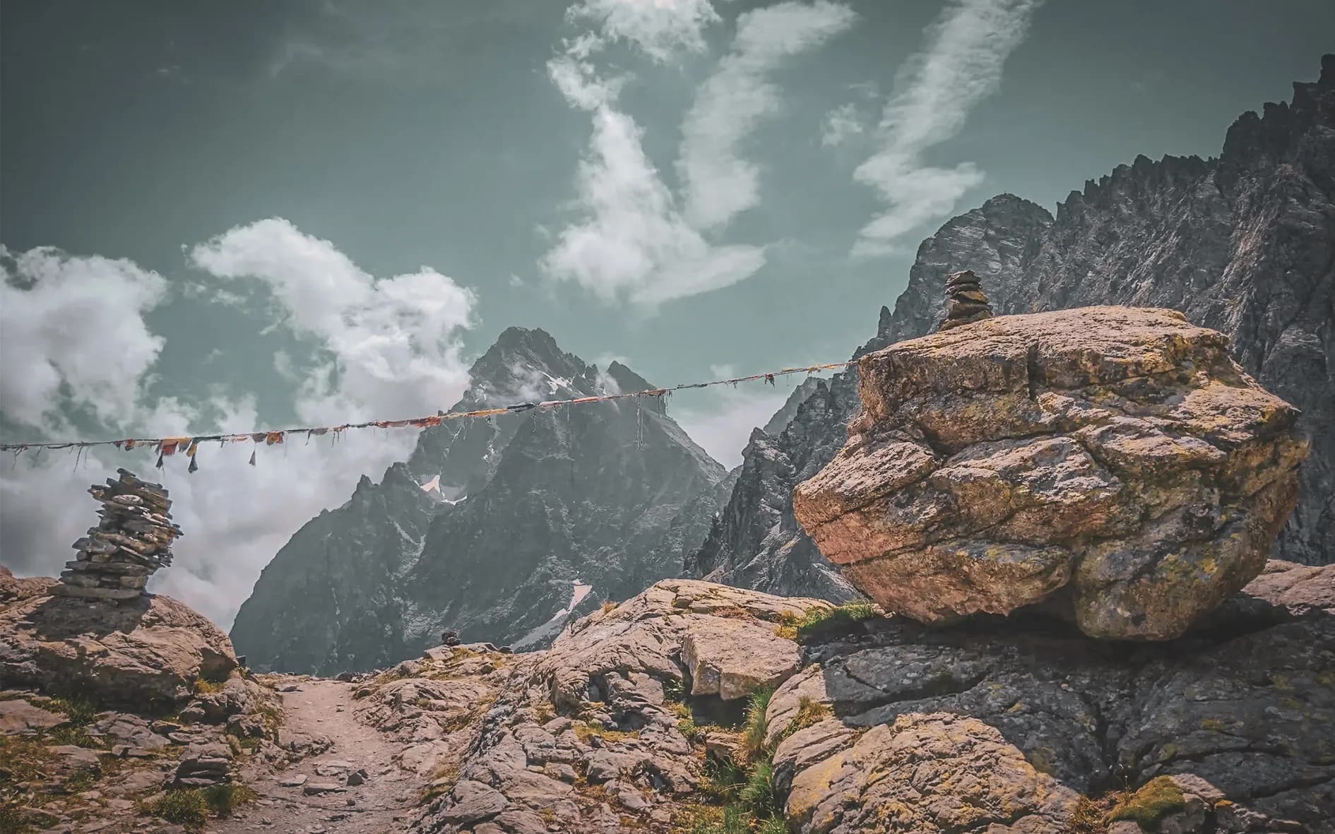 Un paysage alpin époustouflant avec des montagnes majestueuses, des nuages et des cairns de pierre.