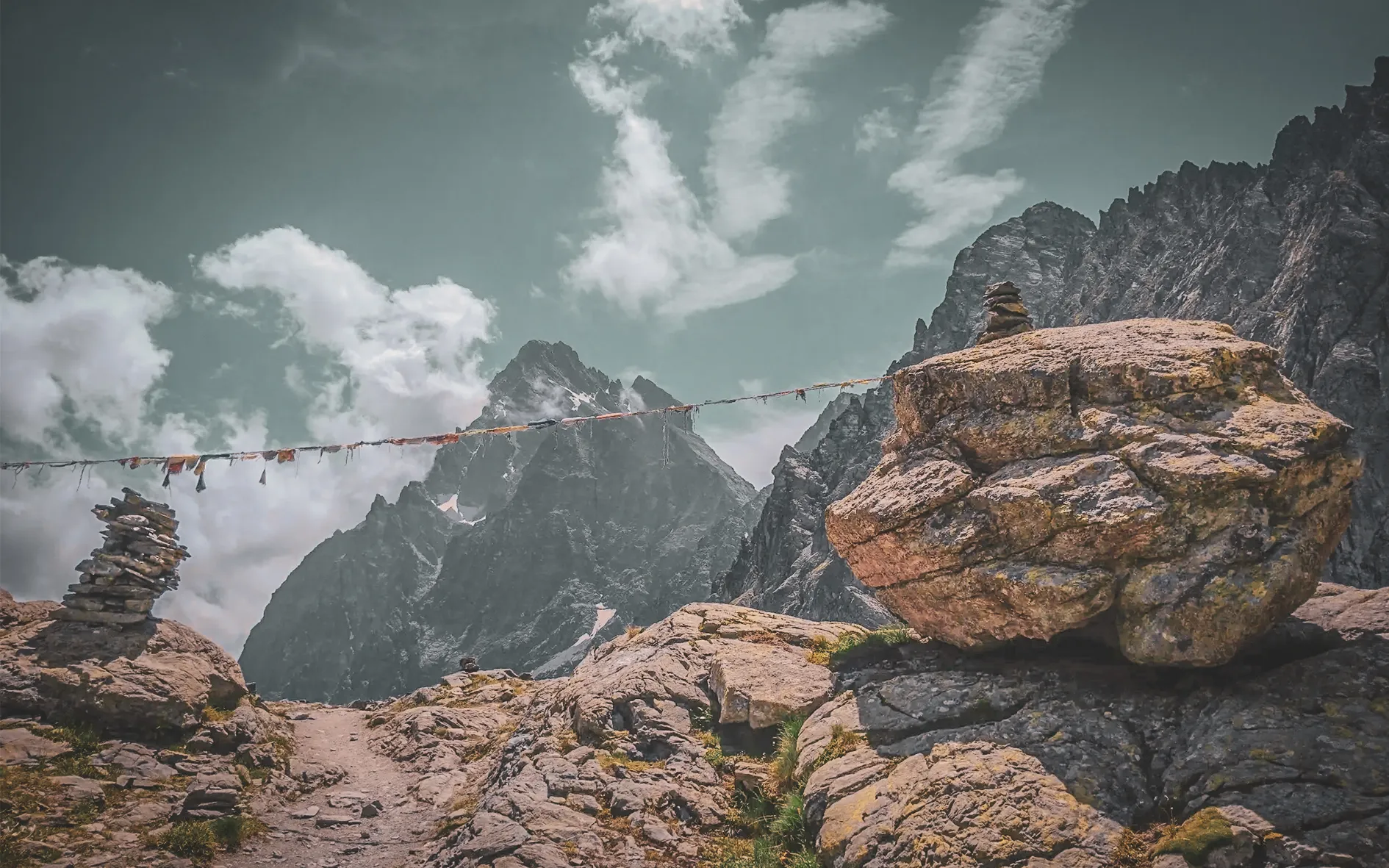 Un paysage alpin époustouflant avec des montagnes majestueuses, des nuages et des cairns de pierre.