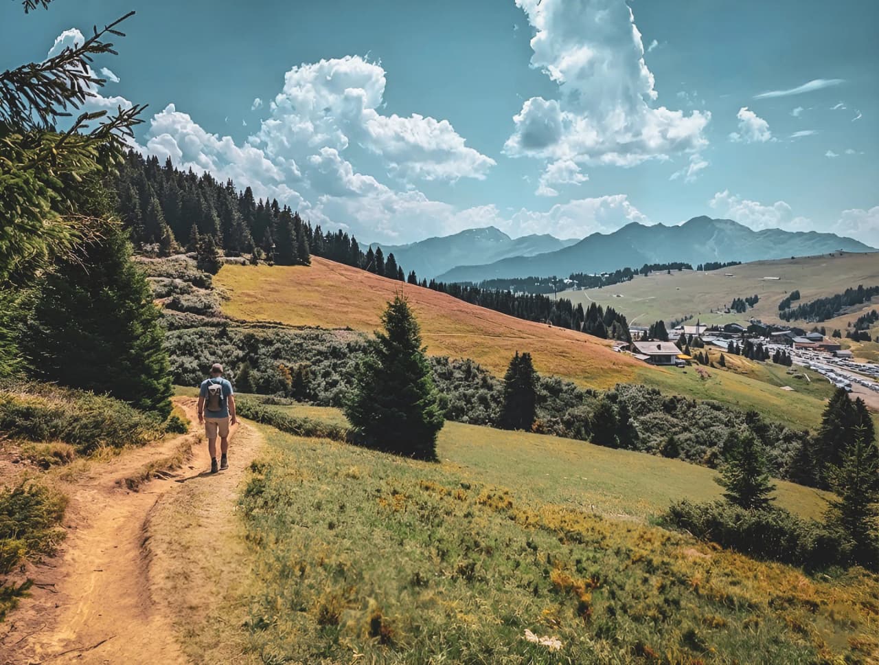 A hiker walks along a green path, facing magnificent Alpine scenery.