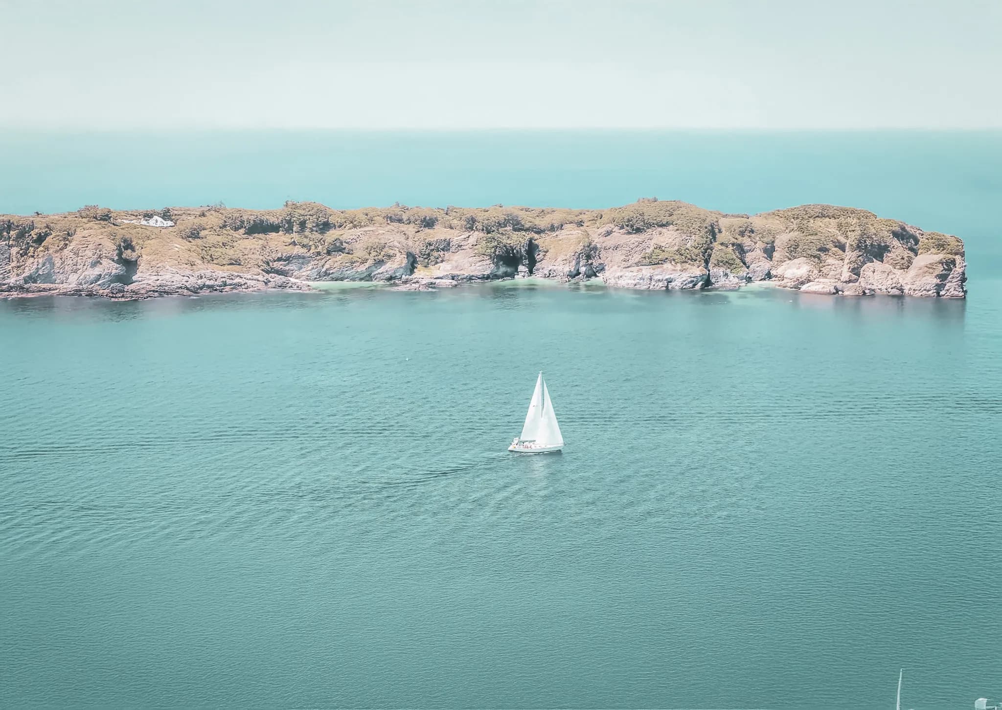 Voguez à la voile sur des eaux turquoises, avec une île en toile de fond. Une invitation à l’évasion.