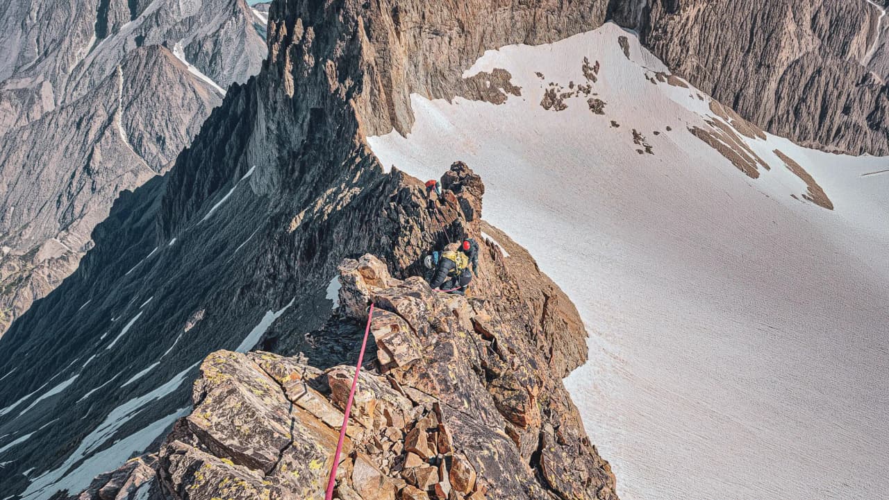 Grimpeurs sur une crête escarpée, avec des sommets majestueux en arrière-plan et la neige étincelante.