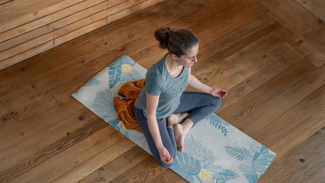 Woman meditating peacefully on a yoga mat, in an enchanting natural wood setting.