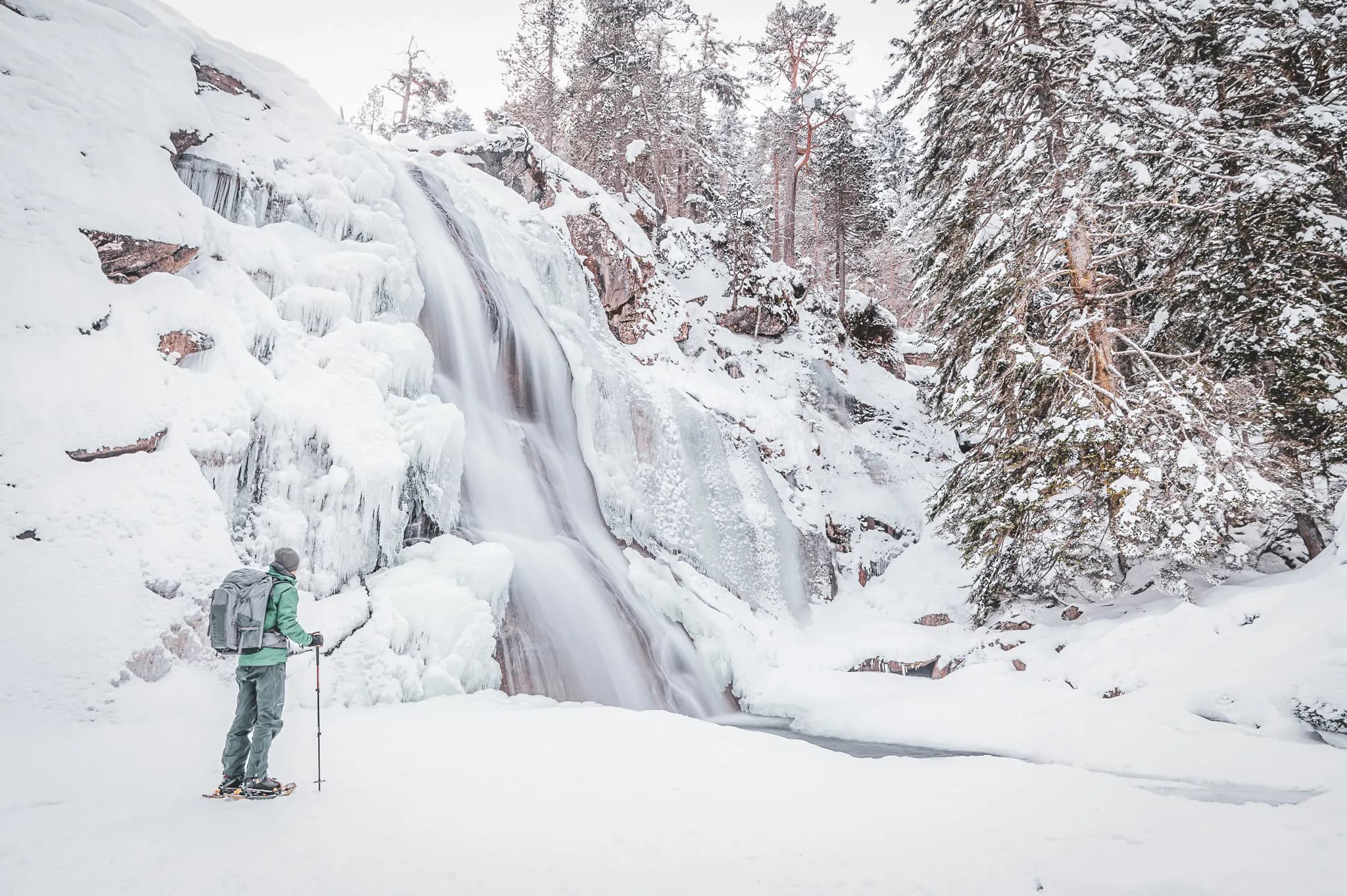 Hiker admiring a frozen waterfall in the heart of the snow-covered Pyrenees. Guaranteed to amaze!