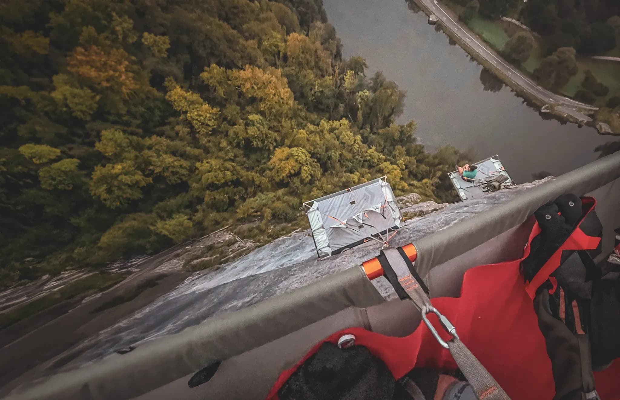 Vue vertigineuse depuis un portaledge, surplombant une forêt colorée et une rivière sinueuse.