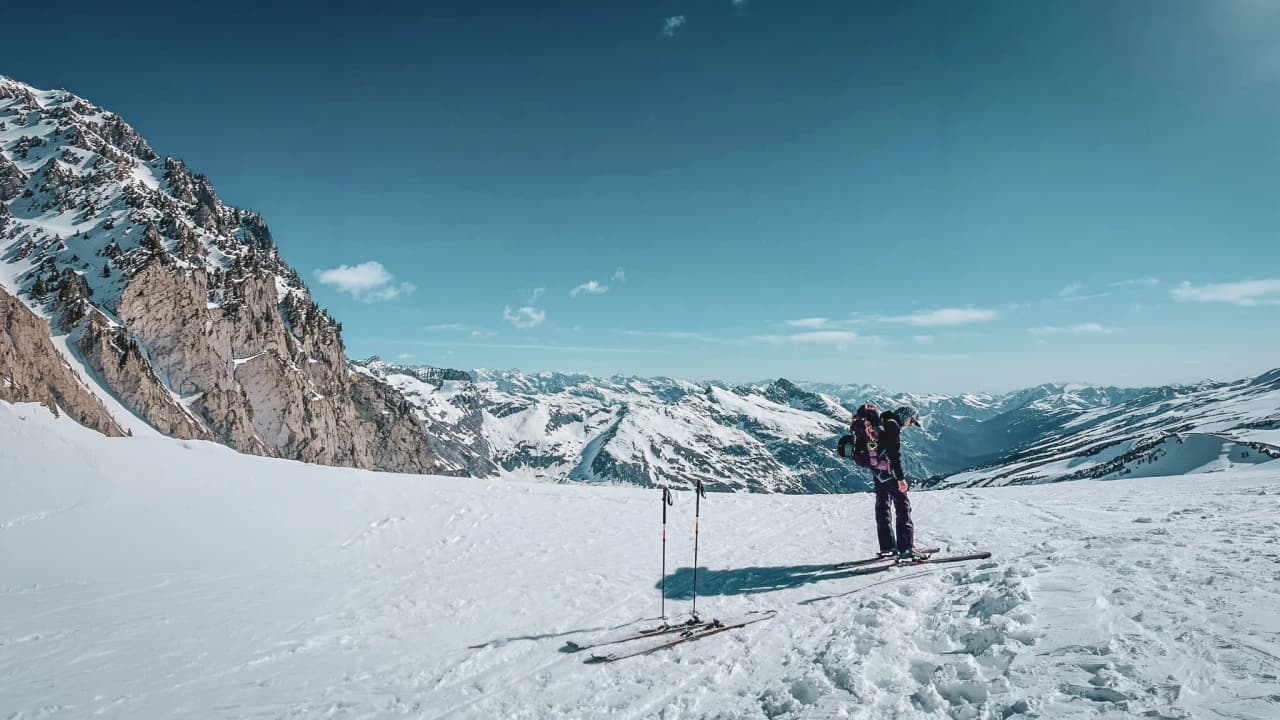 A skier contemplating a majestic panorama of glaciers and mountains under a blue sky.