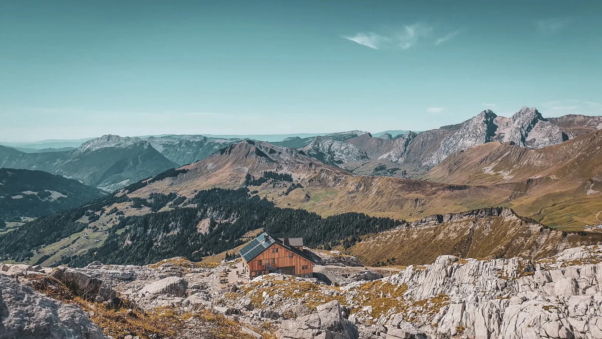 Refuge alpin niché dans un paysage montagneux, avec sommets majestueux et vaste vallée verdoyante.