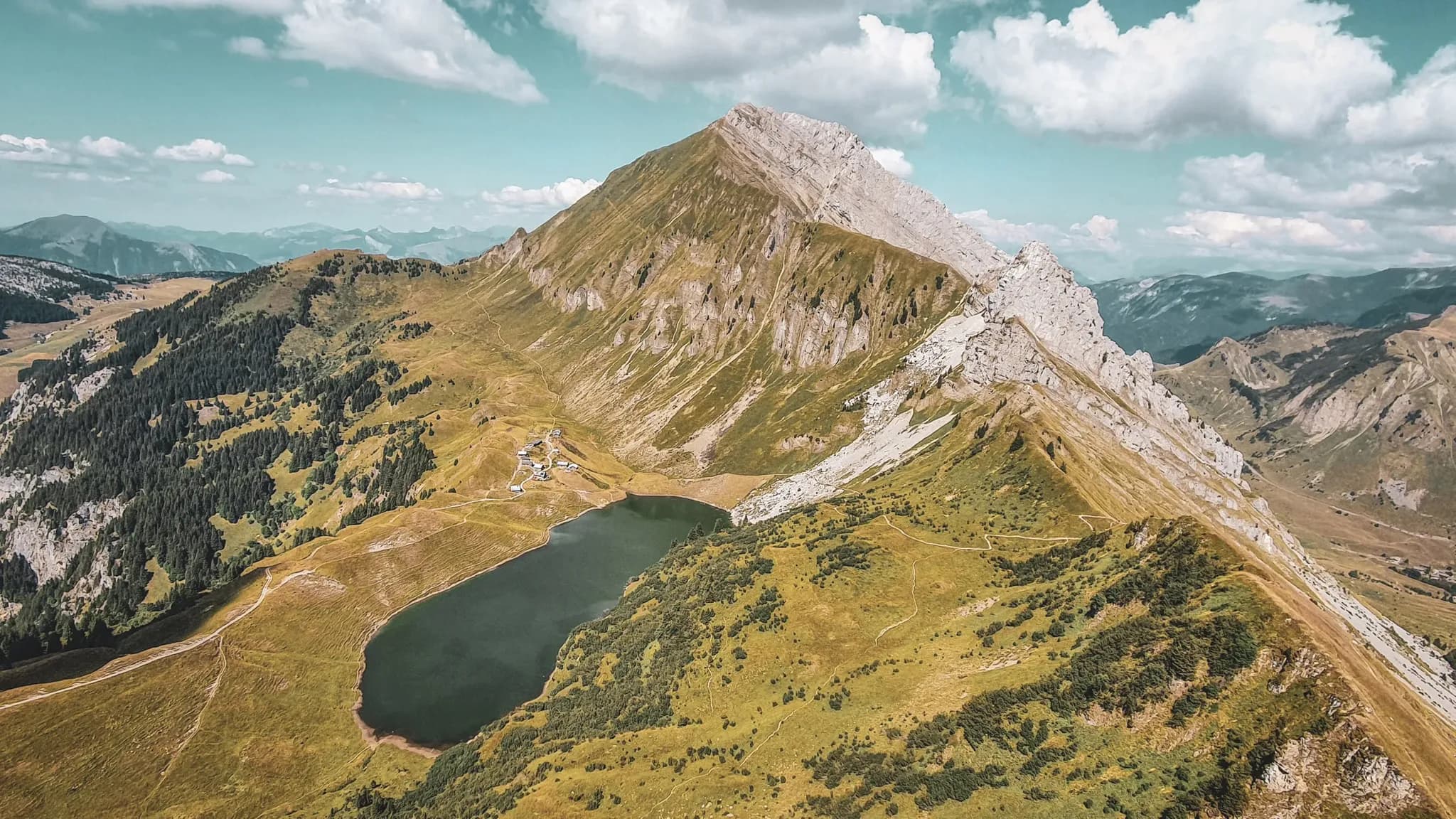 Un panorama magnifique des Aravis, entre montagnes majestueuses et lac paisible entouré de verdure.