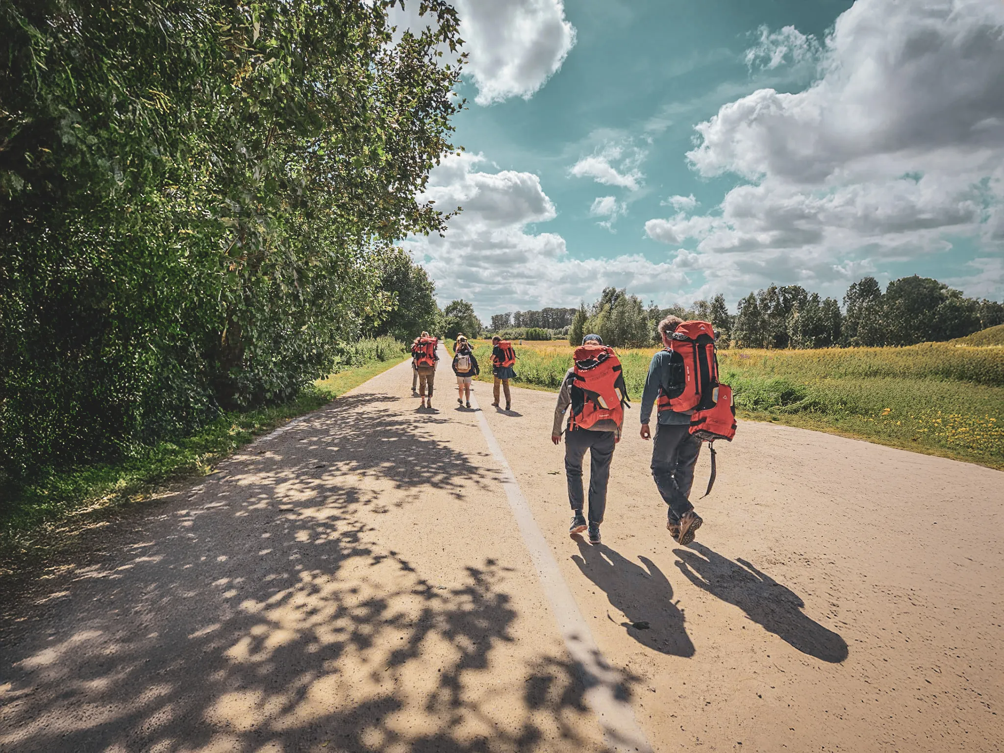 Groupe de randonneurs en packraft marchant sur un chemin, entouré de verdure et de ciel bleu.