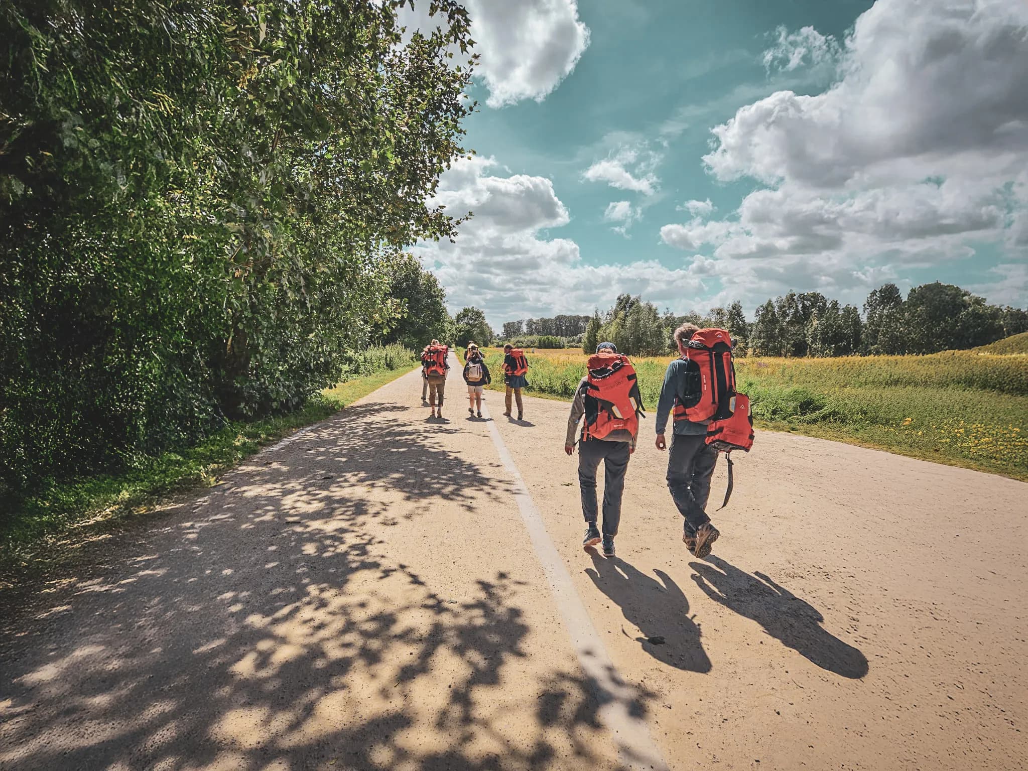 A group of packraft hikers walking along a path, surrounded by greenery and blue skies.
