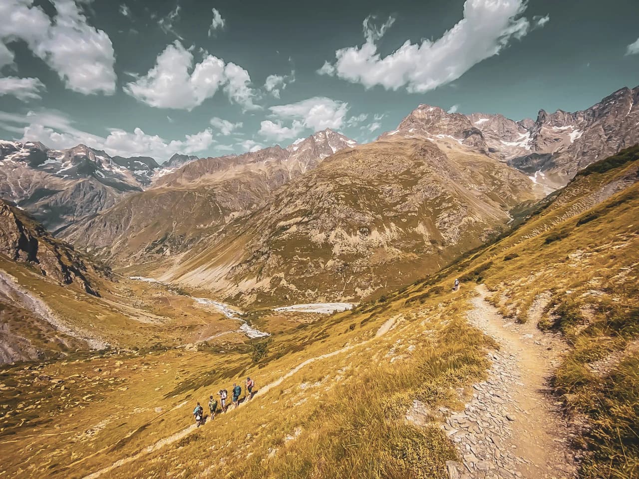 Randonneurs progressant sur un sentier montagneux, entourés de sommets majestueux et de vallées.