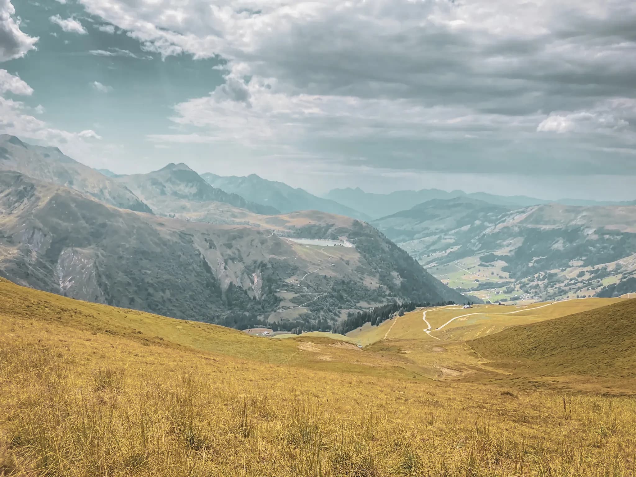 Uitgestrekte gouden weiden en majestueuze bergen onder een bewolkte hemel, een uitnodiging om te reizen.
