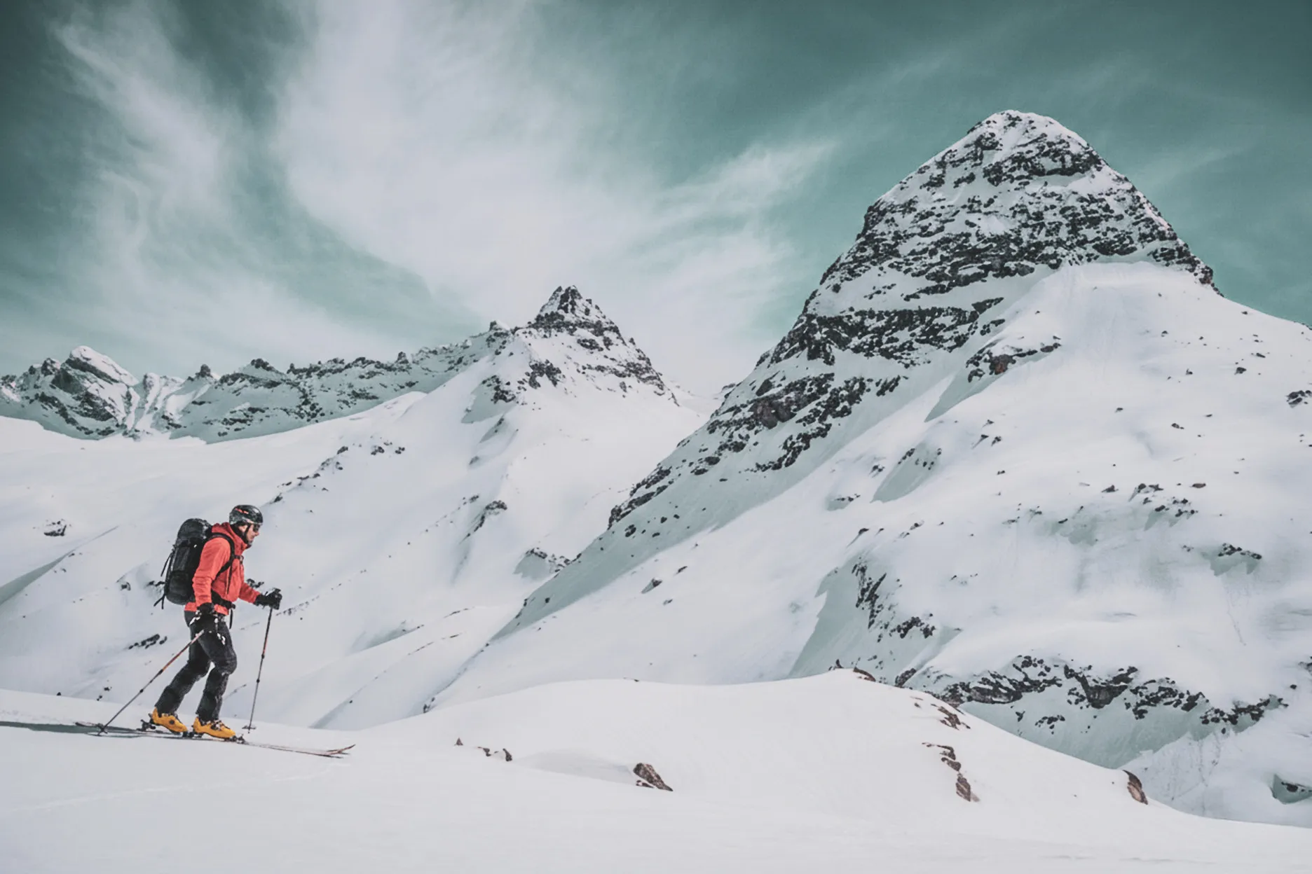 Skier in full ascent on snow-covered glaciers, majestic peak in background.