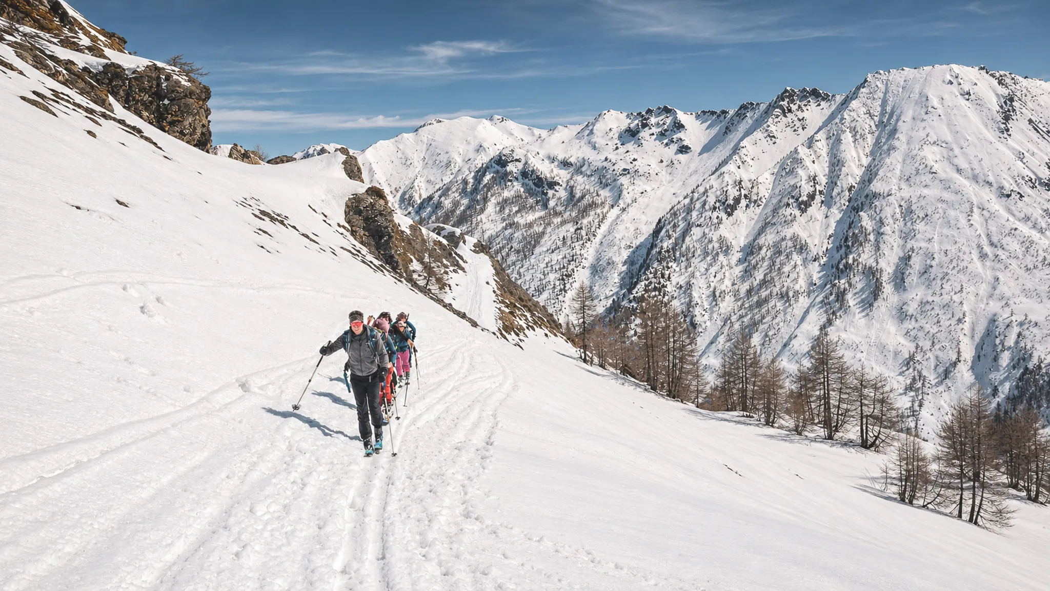 Groupe de randonneurs skiant sur une neige immaculée avec les sommets majestueux en arrière-plan.