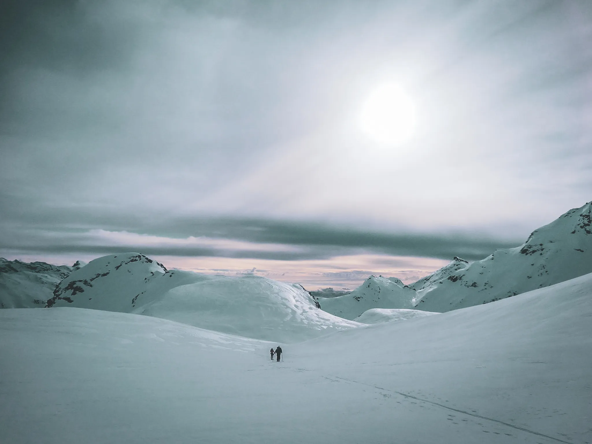 Two skiers light up in the heart of a majestic glacial landscape, under a cloudy sky.