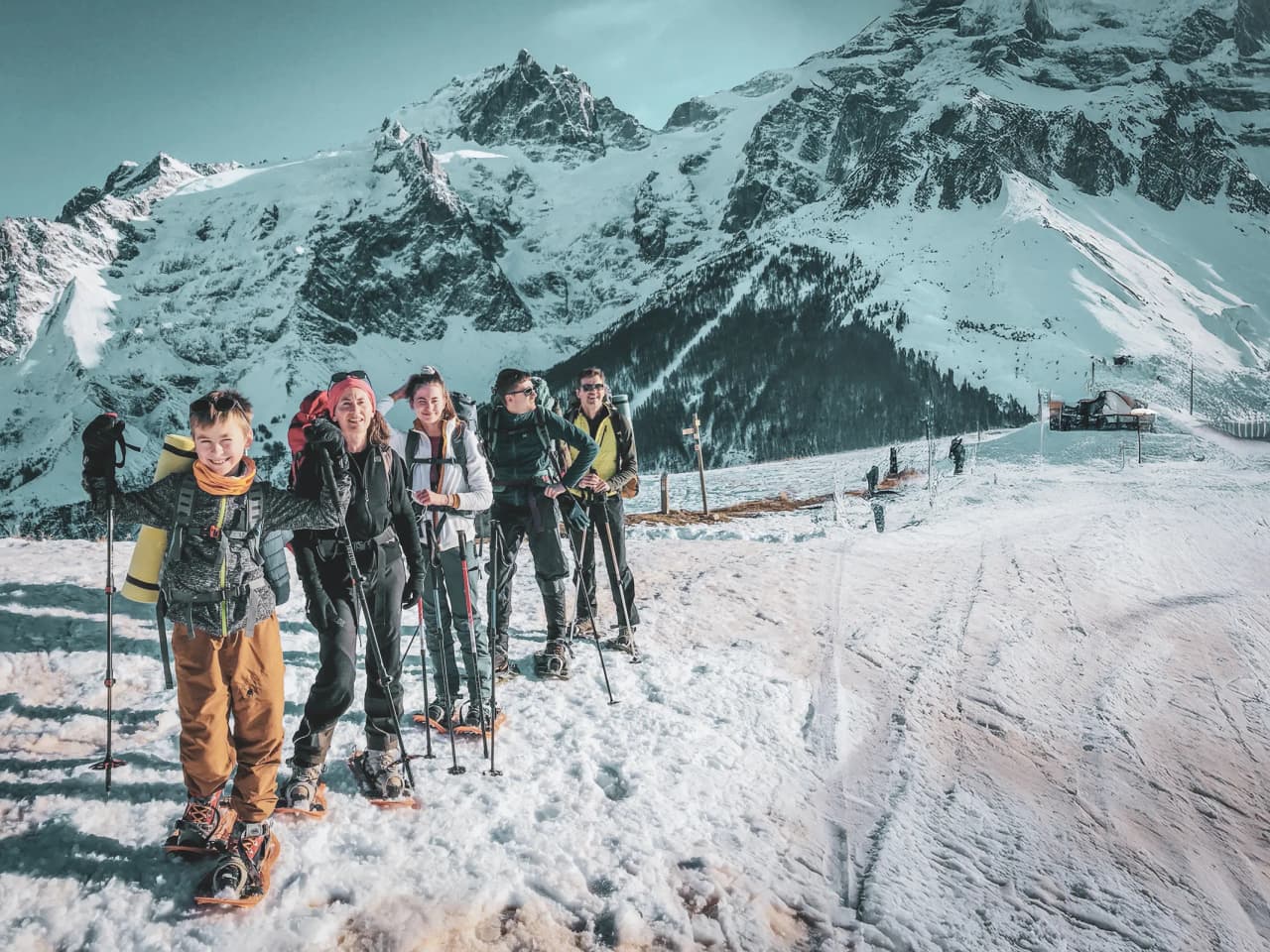 Een vrolijke groep op sneeuwschoenen in een besneeuwd alpenlandschap, met majestueuze bergtoppen op de achtergrond.