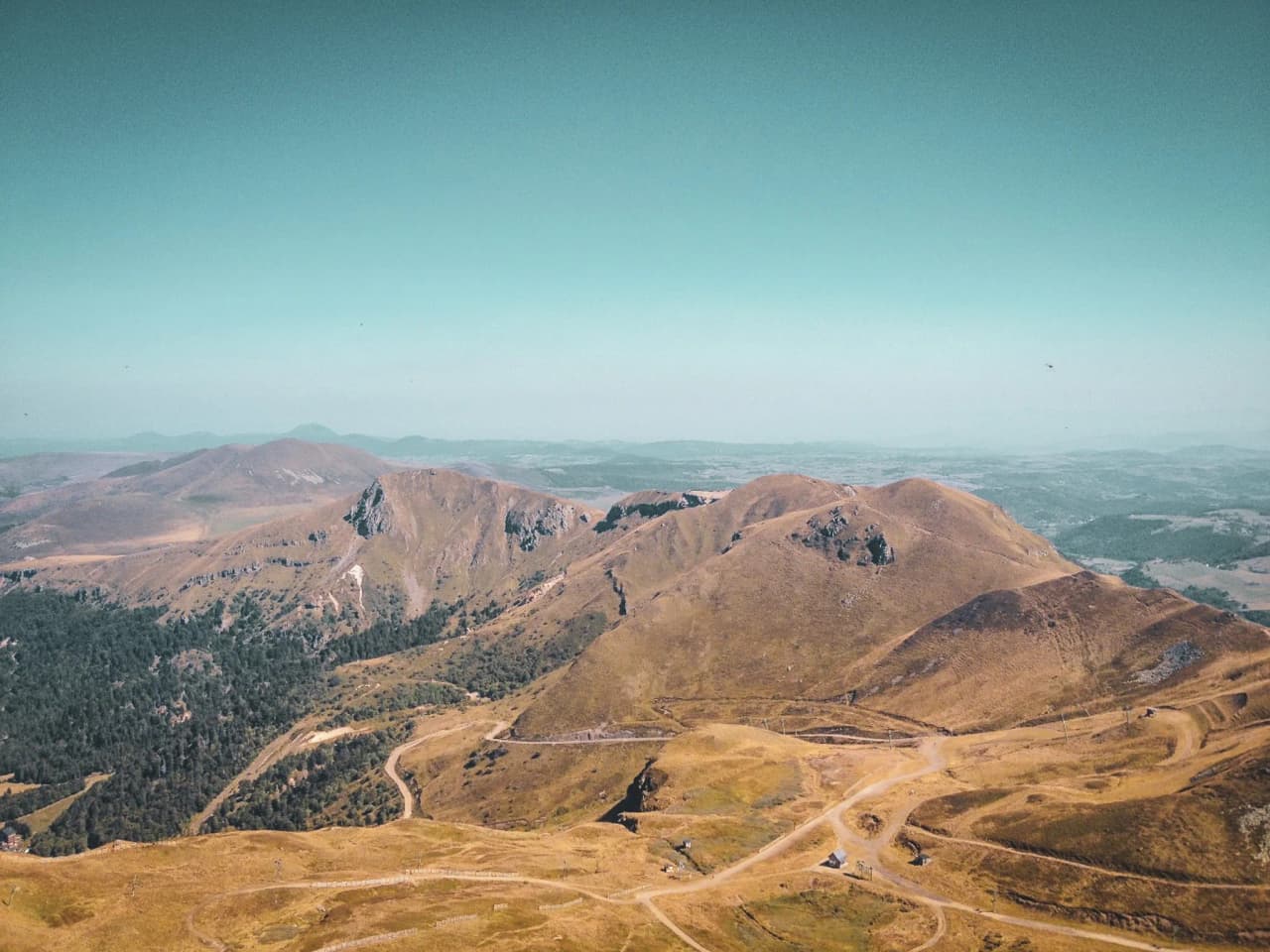 Het berglandschap van het Centraal Massief, met vulkaantoppen en weelderige groene valleien onder een blauwe hemel.