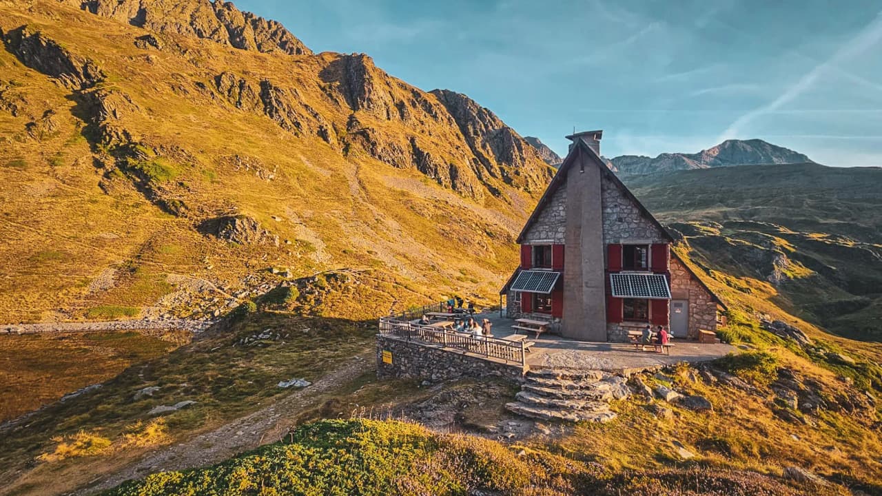 A picturesque mountain hut under an azure blue sky, surrounded by impressive golden valleys.