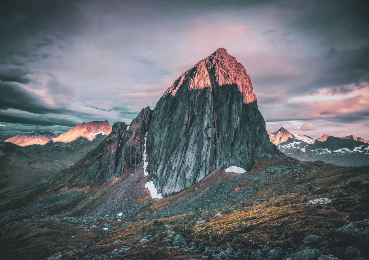 Een majestueuze berg met uitzicht op spectaculaire fjorden onder een dramatische hemel. Ontsnapping gegarandeerd.
