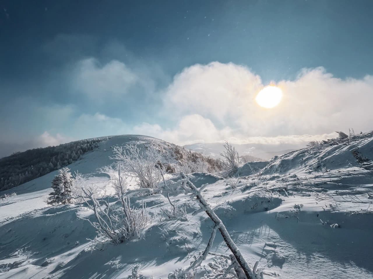 A vast snow-covered landscape in the Vosges, bathed in bright sunshine and soft clouds.